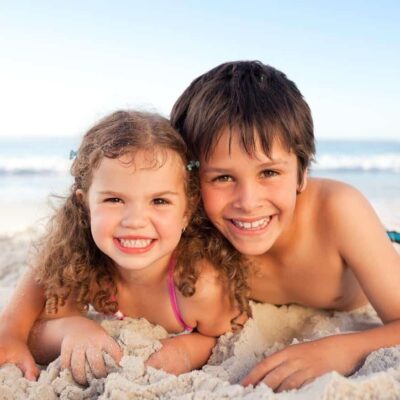 siblings laying on beach smiling together