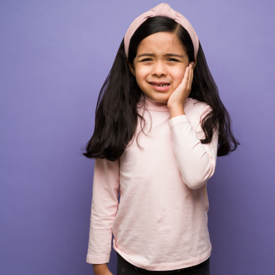 Find out how to save a knocked out tooth 3 Little girl holding cheek, looking distressed, representing how to save a knocked out tooth